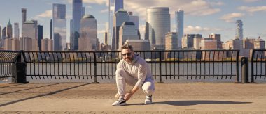 Sporcu antrenmana hazırlanıyor. Ayakkabılarını giyip yerde oturuyor. Spor ayakkabılarını bağlayan sporcu. Atletik ayakkabılar. Spor ayakkabısı kravat bağcıkları dışarıda. Spor ayakkabılarının bağcıklarını bağlayan spor adamı. Yarışa hazır..