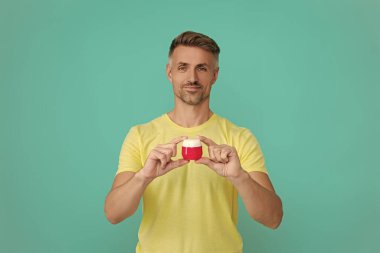 Günlük alışkanlık ve kişisel bakım. Cilt güzelliği. Erkek güzellik kozmetiği. Erkek kozmetik ürünü sunan adam. İzole edilmiş yüz kremi gösteren adam. Olgun adam cilt kremi kullanır. Cilt bakımını takip et.