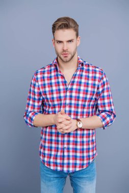 Gündelik giyinen milenyum adamı. Erkek güzeli. Yakışıklı genç adam. Sıradan gömlekli bir adamın portresi. Gri üzerinde kollarını çapraz tutuyor. Tıraşsız erkek derisi. Erkek güzelliği ve saç stili.