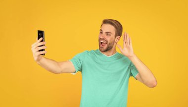 Akıllı telefondan video blogu yapan adam. Telefonla blog yazıyorum. Etkileyici ya da danışman. Mutlu adam selfie çekiyor. Erkek blogcu. Cep telefonlu vlogger Merhaba işareti göster.