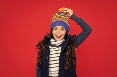 Olumlu duygularını ifade et. Kış modası. Şapkalı, kıvırcık saçlı, şaşkın çocuk. Kırmızı arka plandaki genç kız. Kalın giysiler giyen çocuk portresi.