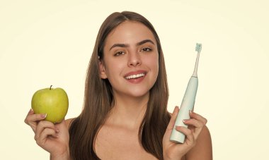Beyaz gülüşlü, dişlerini elektrikli diş fırçasıyla fırçalayan, elma tutan kadın..