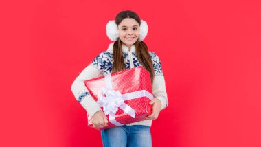 Noel tatili. Kış kulaklıklarıyla noel hediyeli mutlu genç kız. Genç kız Noel hediyesi olarak kırmızı arka planda izole edilmiş..