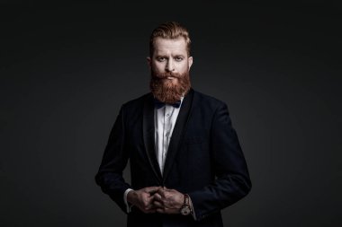 Sakallı damat kendinden emin ve hırslı hissediyor. Smokinli erkek giysili adam Griler 'de izole edilmiş. Smokinli adam resmi erkek giyim bölümünde. Yakışıklı sakallı adam smokin giyer. Şık smokin papyonu. Gerçek zarafet.