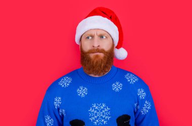 Şaşırmış Noel Baba 'nın portresi kırmızıda izole edilmiş. Noel Baba şapkası stüdyosu giyen kafası karışmış sakallı bir adam. Noel partisi. Yılbaşı arifesi kutlaması. Kış tatili.
