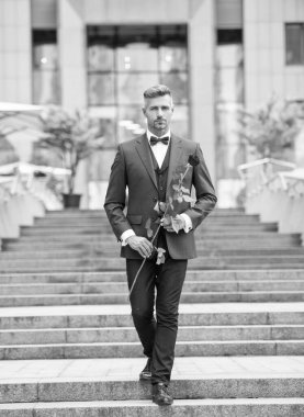 Smokinli şık bir adam. Smokin giymiş papyonlu bir adam dışarıda yürüyor. Kırmızı güllü yakışıklı smokinli adam..