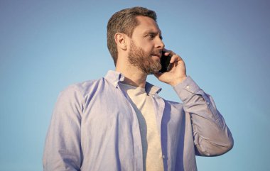 Telefonda erkek erkeğe konuşma. Adam akıllı telefondan konuşuyor. Gökyüzü arka planında insan iletişimi.