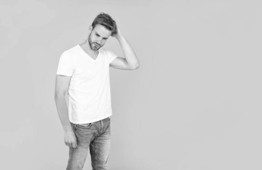 Erkek güzelliği. Beyaz gömlekli kıllı adam. Sakallı genç adam sarı arka planda kıllara dokunuyor. Saç ve sakal bakımı. Kendine güvenen ve yakışıklı, tıraşsız adam. Erkek modası.