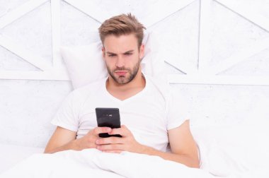 Genç adam yatakta telefonda konuşuyor ya da mesajlaşıyor..