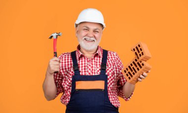 cheerful old aged man worker in helmet on yellow background.
