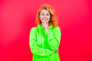 Kız havalı görünüyor. Minimum giysi. Pembe üzerine izole edilmiş kapüşonlu günlük kıyafetler giyen kızıl saçlı kadın. Yaşam tarzı konsepti. Kapüşonlu kadın model. Çekici bir kadının şık bir görünüşü var. Modaya uygun..