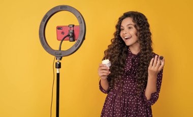 Uzun kıvırcık saçlı mutlu çocuk blogda pudra fırçası videosu çekiyor.