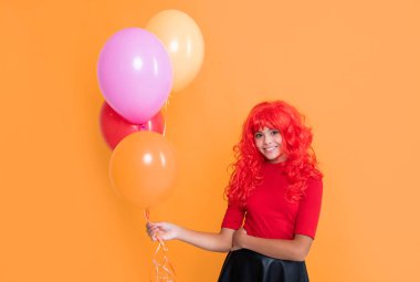 Çocuk sarı arka planda parti balonuyla gülümsüyor.