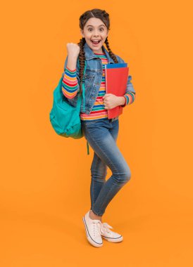 Kazanan jest yaptığı için heyecanlı bir kız. Genç kız okula geri döndü. Kitapları sarı arka planda tutan genç bir kız. Okul eğitimi.