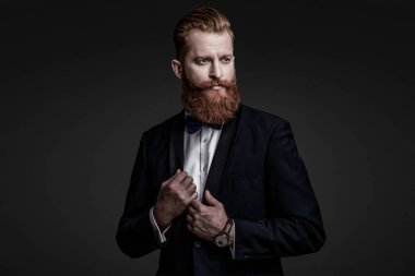 Yakışıklı sakallı adam smokin giyer. Şık smokin papyonu. Sakallı damat kendinden emin ve hırslı hissediyor. Smokinli erkek giysili adam Griler 'de izole edilmiş. Smokinli adam resmi erkek giyim bölümünde. Mükemmel biçim.