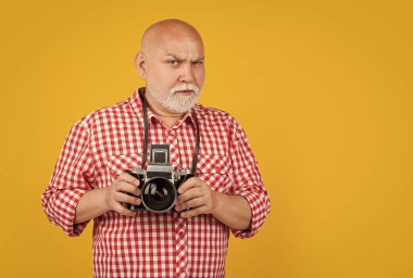 sad old man with retro photo camera on yellow baqckground.
