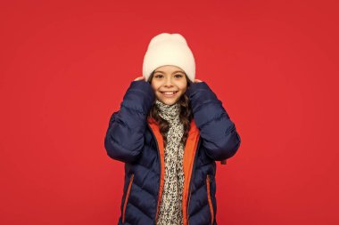 cute positive kid with curly hair in puffer jacket and hat. teen girl on red background. portrait of child wearing warm clothes with scarf. express positive emotion. winter fashion. clipart