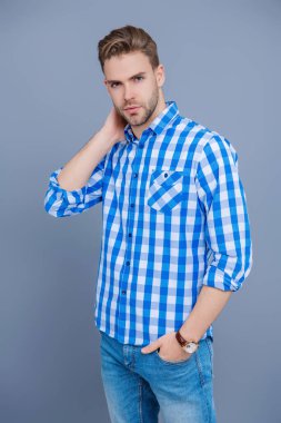 Kareli gömlek giyen milenyum adamı. Milenyum erkeğinin gündelik tarzı. Sıradan tişörtlü bir adamın portresi. Tıraşsız adamın zarif portresi. Gri yolda izole edilmiş bir adam. Günlük düğmeli gömlek..