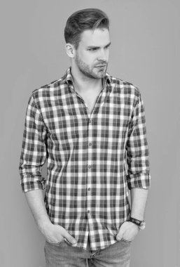 Traşsız, şık bir adamın stüdyo fotoğrafı. Kirli sakalı olan beyaz bir adam. Gri arka planda kareli gömlekli şık bir adam izole edilmiş. Havalı tişörtlü adam..