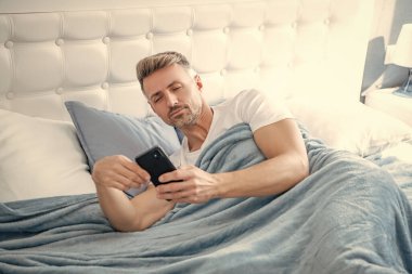 mature man in bed chatting on phone. clipart