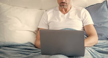 mature man working on laptop in bed. business online.