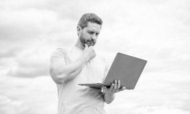 Düşünen adam gökyüzü arka planında dizüstü bilgisayarda çalışıyor..