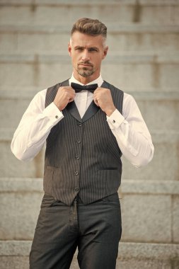 Papyonlu, olgun, zarif bir adam. Resmi giysili, kır saçlı bir adam. Smokinci damat..