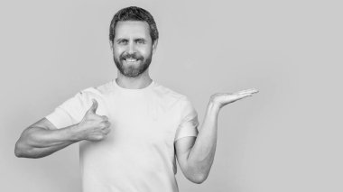 Arka planda reklam sunan mutlu adam, başparmağını kaldır. Stüdyoda reklam sunan adam. Reklam sunan adamın fotoğrafı. Reklam sunan adam sarı üzerine izole edilmiş..