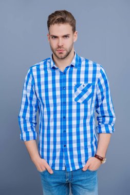 Tıraşsız adamın zarif portresi. Gri yolda izole edilmiş bir adam. Kareli gömlek giyen milenyum adamı. Milenyum erkeğinin gündelik tarzı. Sıradan tişörtlü bir adamın portresi. Erkek giyim.