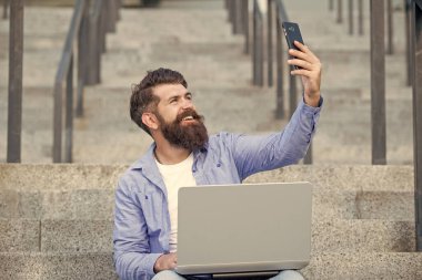 Mutlu adam cep telefonundan selfie çekiyor. Merdivenlerde cep telefonu kamerasına gülümseyen sakallı adam. Mobil internet kullanarak. Mobil iletişim.