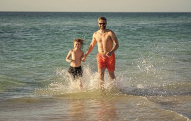 Baba ve oğulun denizde özel anları vardır. Baba oğul maceraları. Baba, baba, oğul deniz sahilinde koşuyor. Baba oğul, yaz tatilinin tadını çıkarıyor. güçlü ilişki.