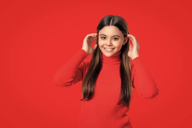 Sıradan bir tarz. Tarz sahibi kızın uzun saçları var. Genç tek renkli moda tarzında. Kız için tarz. Kırmızıda izole edilmiş mutlu genç kızın portresi. Genç kız kameraya bakıyor. Boşluğu kopyala.