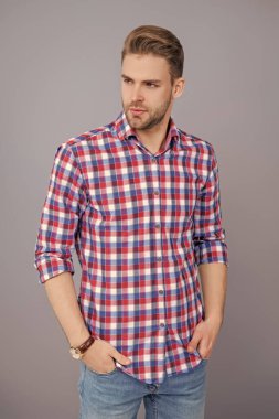 Gri yolda izole edilmiş bir adam. Kareli gömlek giyen milenyum adamı. Milenyum erkeğinin gündelik tarzı. Sıradan bir tişörtle genç bir adamın portresi. Tıraşsız adamın şık bir portresi. Model pozu.