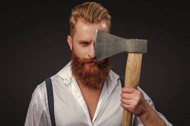 Erkek vahşeti. Antika pantolon askılı, eski tip bir gaddar adam. Siyaha izole edilmiş baltalı askılı vahşi bir adam. Saçları kızıl saçlı, olgun bir adam. Acımasız erkek modası. Berberlik konsepti.