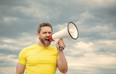 man in yellow shirt speak in megaphone on sky background.