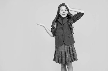 happy childhood. child presenting product, copy space. amazed teen girl carry backpack. back to school. knowledge day. concept of education. kid in uniform on yellow background. september 1.