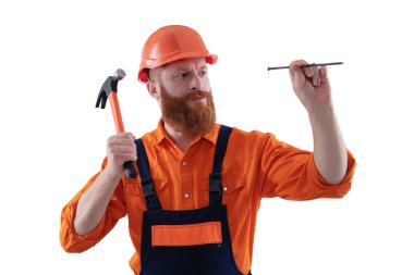 Adam çekiç çivisi tutuyor. Marangozluk ve onarım. Üniformalı tamircinin çekici var. Çekiçle sakallı tamirci. Marangoz, beyaz çiviyle tamir ediyor. Tamirci. DIY onarımları.