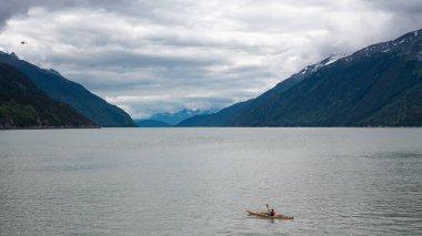 Kanodaki adam Alaska dağ zirvesine bakıyor. Chilkoot körfezi nehri. Chilkoot koyuyla birlikte dağ manzarası. Manzaralı bir manzara. Dağ ve nehir doğayla iç içe. Seyahat hedefi.