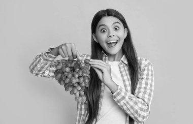 amazed teen girl with grapes fruit on yellow background.