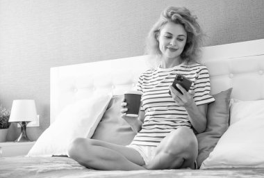 Telefonda internette kahve sörfü yapan neşeli bir kız. Kız evde telefonuyla internette sörf yapıyor. Kızın evinde internet sörfü.