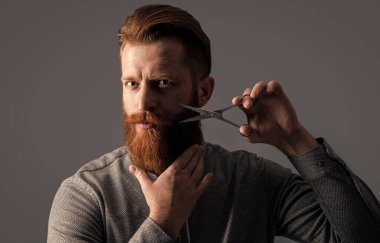 Kuaförlük konsepti. Adam berber kuaförlüğü gri stüdyo geçmişinde izole edilmiş. Berber makasıyla kuaförlük yapan adam. Kuaför stüdyosunda berber. Berber adam kuaförlük için makas tutuyor..