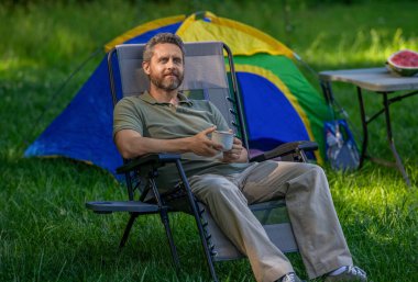 Kamp çadırı. Kahve fincanı. Ormanda sabah kahvesi içen bir adam. Yaz günü doğa yürüyüşçüsü. Yaz kampı ve doğa tatili. Yaz kampındaki adam. Kamp macerası. Yürüyüş kavramı.