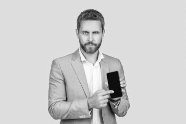 Olgun adam telefon ekranını sunuyor. İş adamı gri alanda izole akıllı telefon gösteriyor. Takım elbiseli adam yeni bir uygulama önerdi. Ürün teklifi. Reklam sunumu, kopyalama alanı. Promosyon reklamı.