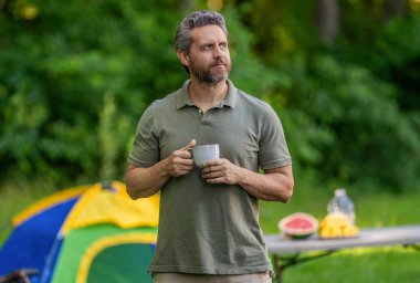 Kamp macerası. Yürüyüş konsepti. Kamp çadırı. Kahve fincanı. Adam ormanda sabah kampı kahvesi içiyor. Yaz günü doğa yürüyüşçüsü. Yaz kampı ve doğa tatili. Yaz kampındaki adam..