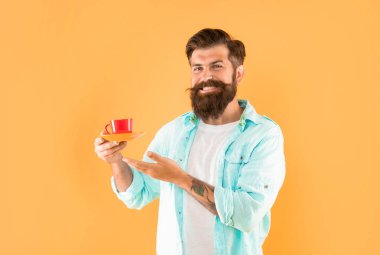 Tıraşsız bir adam sarı arka planda kahve ve içecek gösteriyor..