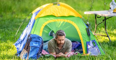 Yürüyüş yaşam tarzı. Sakin ol ve kamp alanında kitap oku. İlham zamanı. Çadırda piknik yapan bir adam. Yaz günü yürüyüş yapan bir adam. Yaz kampı ilhamı. Yaz kampı. Kamp macerası.