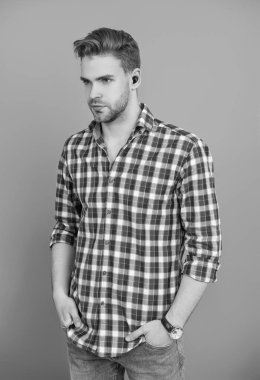 Aleti olan bir milenyum adamı. Kablosuz kulaklıklı bir adam. Adam gri üzerinde kulaklık kullanıyor. Modern kablosuz kulaklıklar. Elsiz kulaklık. Kulaklık cihazı aksesuarı. Kablosuz kulaklık cihazı. Kulaklık Özellikleri.