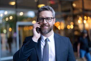 İş görüşmesi. Takım elbiseli adam telefonda konuşuyor. Telefon var. Mobil iletişim. Müzakere çevrimiçi. İş adamı açık havada akıllı telefondan konuşur. Olgun iş adamı telefon görüşmesi yapar. Haberler iyi..