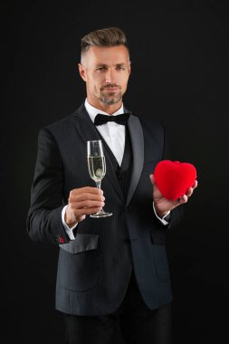 Smokinli ve şampanyalı zengin bir adam. Sevgililer günü indirimi. Zengin adam sevgililer gününü kutluyor. Yürekli bir adam. Sevgililer günün kutlu olsun. Sevgi dolu bir adam siyahta izole edilmiş. Romantik hediyelere bayılırım. Aşk teklifi.