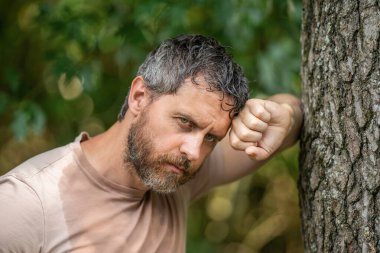 Hispanik olgun ve vahşi sakallı bir adam ormanda ağaçlara yaslandıktan sonra yorgun ve terliyor..